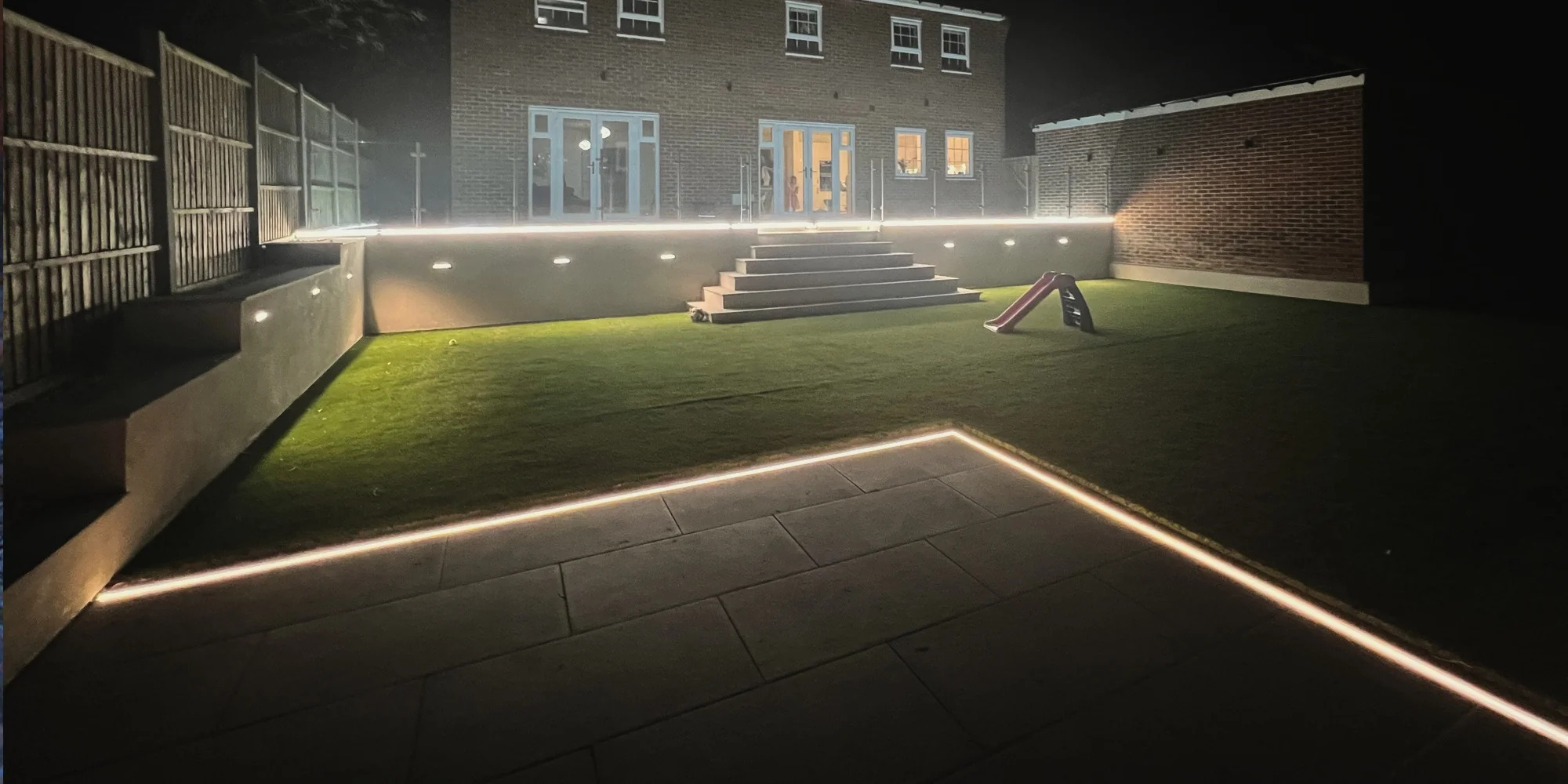 Backyard at night with LED strip lighting on patio steps and lawn
