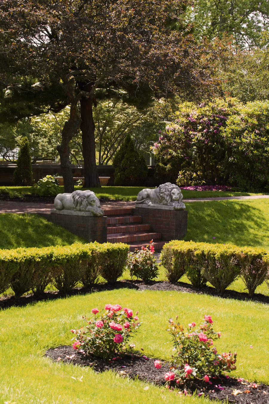 Grand estate garden with lion statues, manicured hedges, rose beds and mature trees