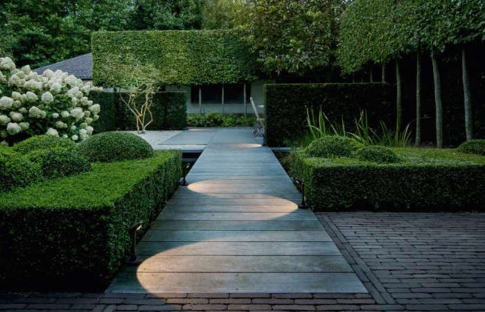 Precisely trimmed formal box hedges with geometric shapes and lit garden path